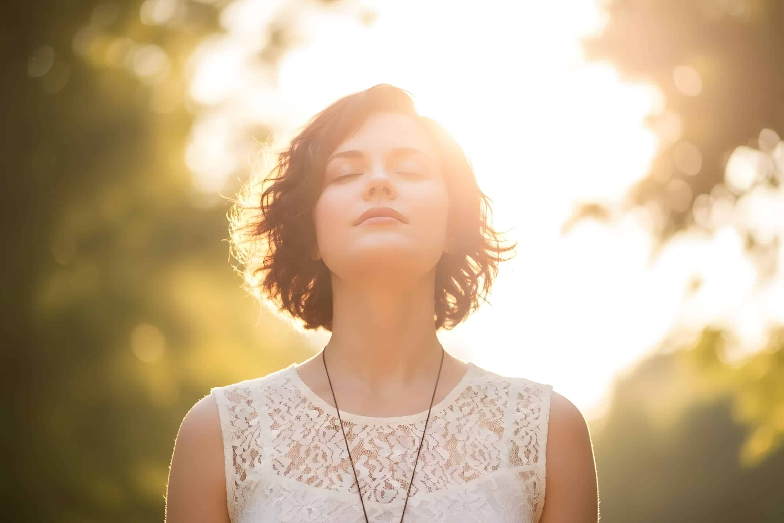 Woman in nature. Sunshine on her. Looks calm.