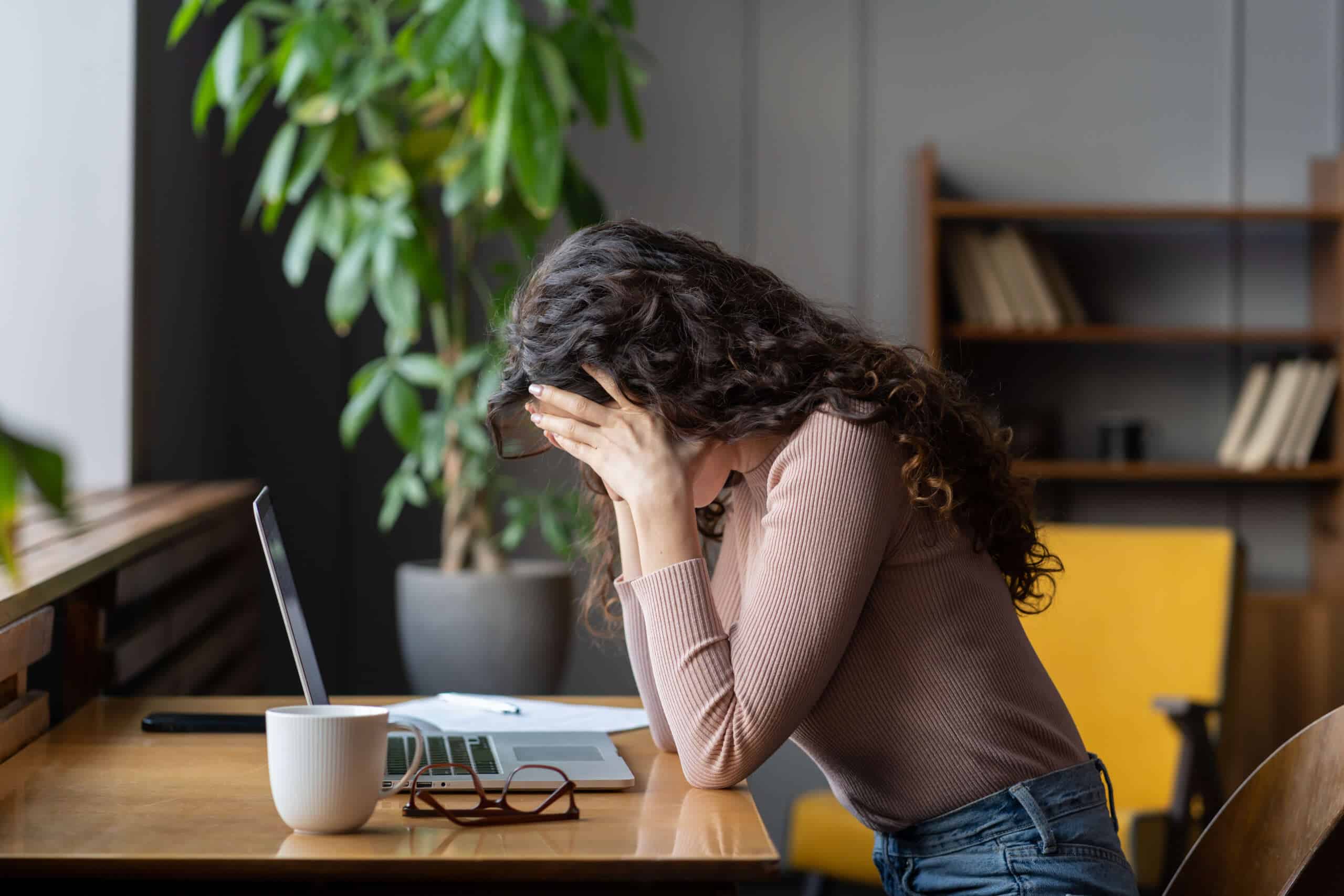 Exhausted unhappy woman sit at laptop hide face in hands tired work overtime suffer from burnout.