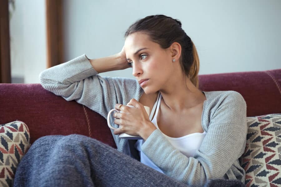Shot of depressed young woman thinking about her problems while drinking coffee on sofa at home.