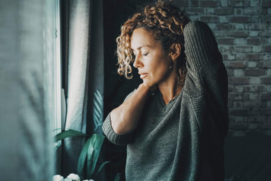 Young mature woman touching his neck for backpain and stretching arms. Concept of healthy and body condition people Female massaging his back for pain and closing eyes to relax. Concept of bad posture