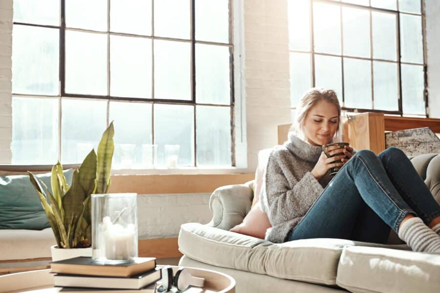 Woman relax in living room, coffee and peace on sofa, content at home with lifestyle and happiness. Female in apartment, happy woman and coffee cup, positive energy and mindset with wellness.