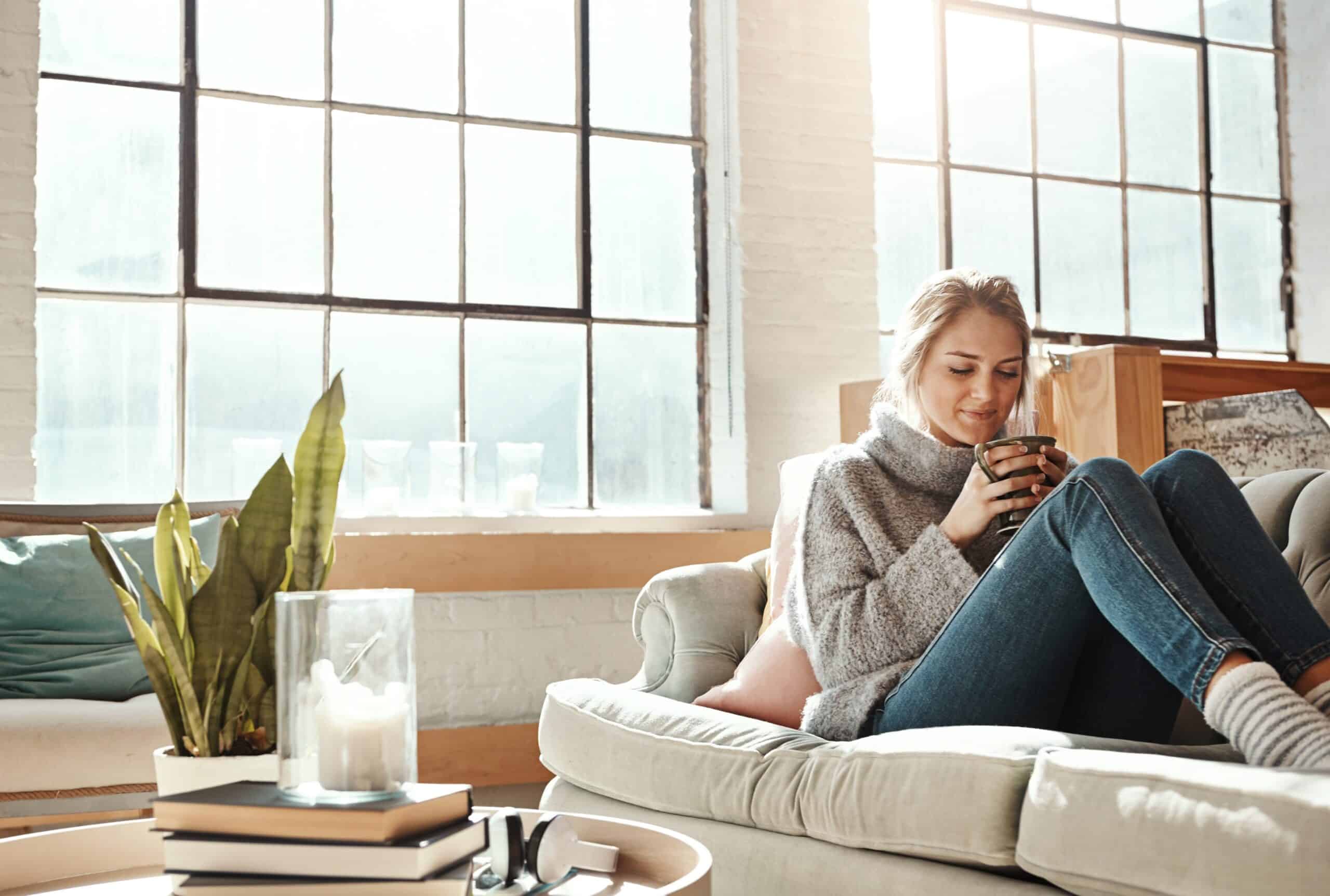Woman relax in living room, coffee and peace on sofa, content at home with lifestyle and happiness. Female in apartment, happy woman and coffee cup, positive energy and mindset with wellness.
